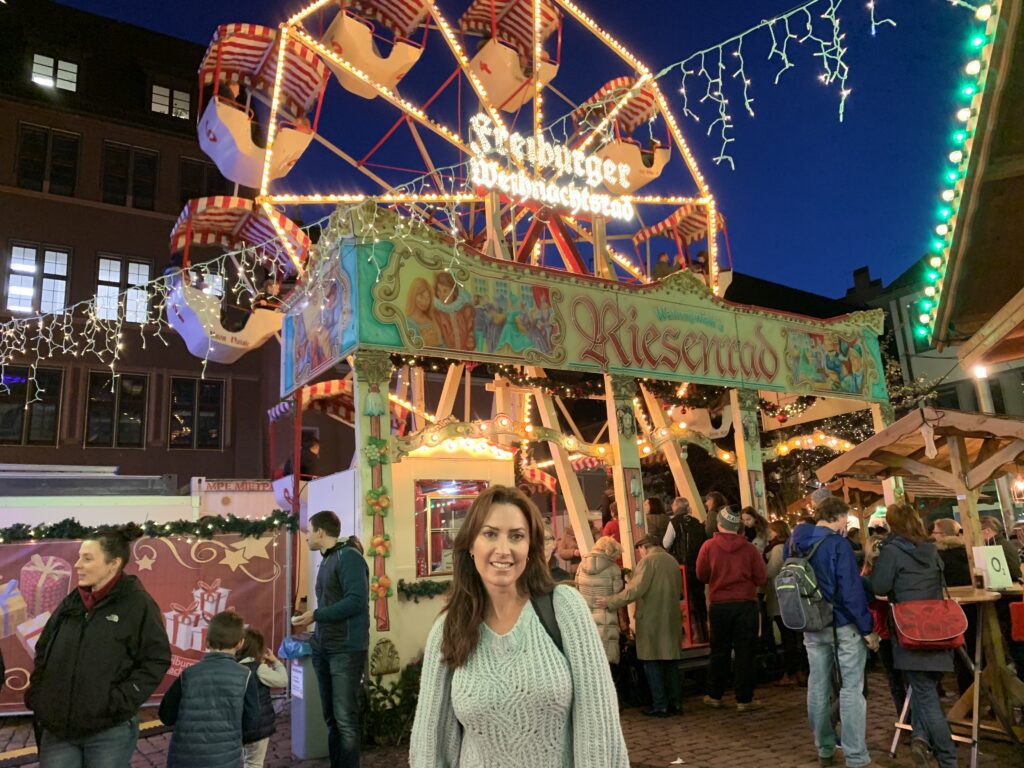 Karen LeBlanc standing in front of a ferris wheel during the night Christmas Market in Freiburg, Germany.