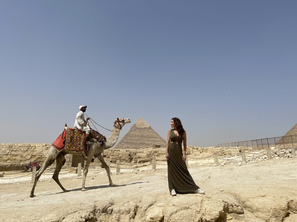A man riding a camel and a woman having a picture to the great pyramid of Giza as background as one of the things to do in Egypt.