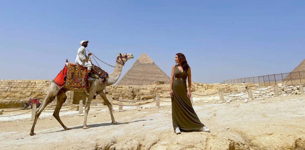 A man riding a camel and a woman having a picture to the pyramid of Giza as background — one of Egypt Bucket List.