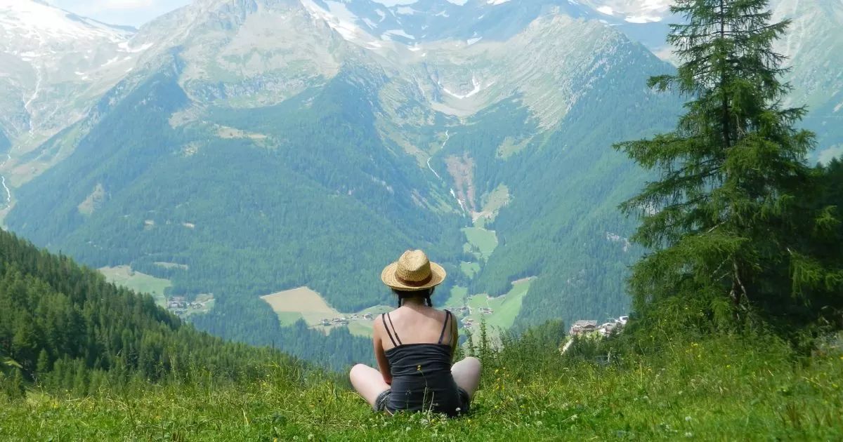 a woman sitting on a hill looking at the View of Mountain Alps
