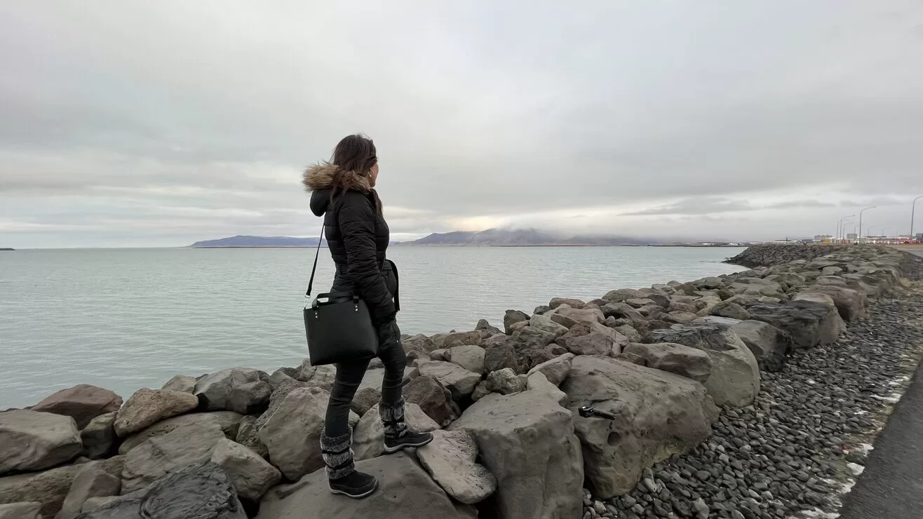 Travel Writer, Karen LeBlanc, aka The Design Tourist, is facing beautiful Mount Esja, standing on the coastline downtown in Rejkjavik, Iceland.