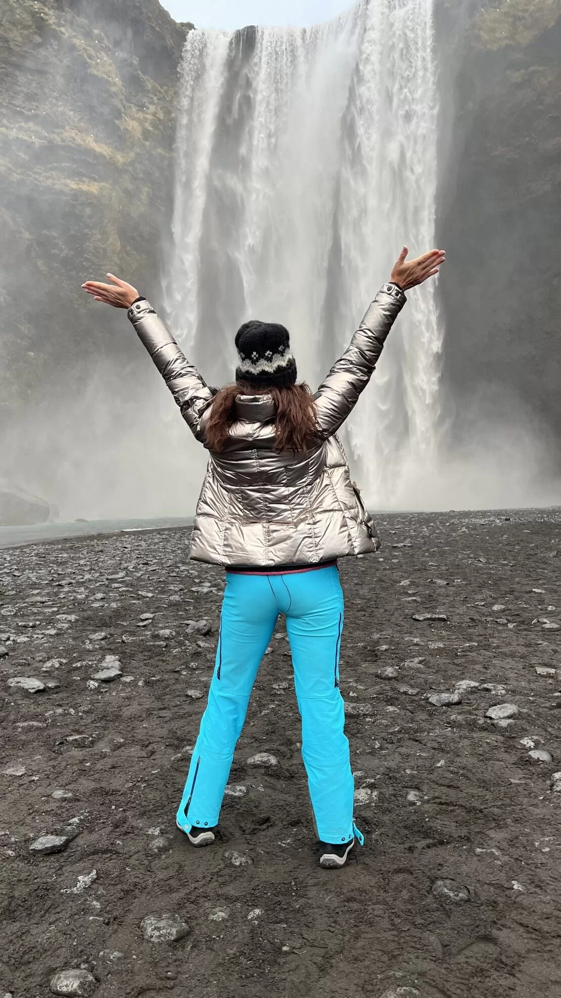 Karen LeBlanc waring a silver coat and a blue pants standing in front of a waterfall
