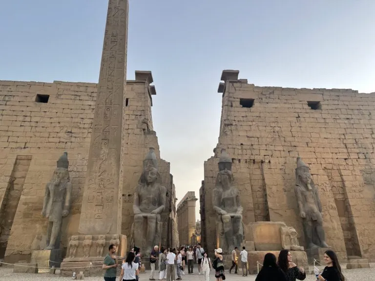 a group of people standing in front of a stone building with Luxor Temple in the background