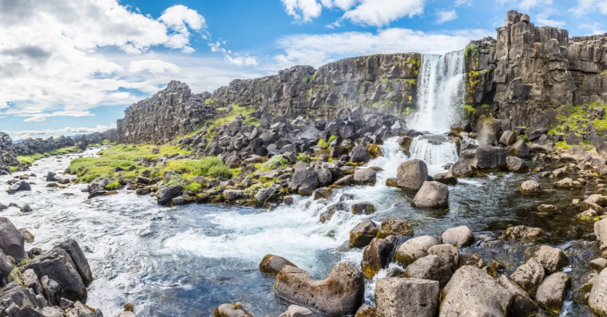 a waterfall over rocks and grass of Þingvellir National Park