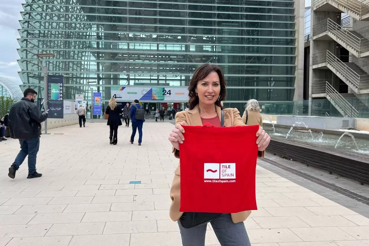 Karen holding a red bag with text reads as 'Tile of Spain' at Cevisama building as background.