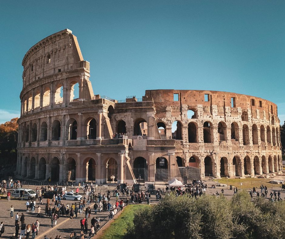The ancient Roman Colosseum with crowds of tourists gathering outside on a clear sunny day in Rome